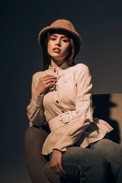 Porträt einer schönen Frau mit stylischem Hut, die auf einem Sessel sitzt und in die Kamera blickt — Stockfoto