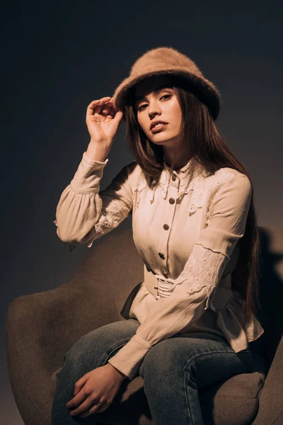 Retrato de mujer hermosa en sombrero elegante sentado en el sillón y mirando a la cámara - foto de stock