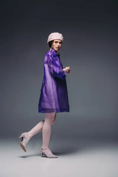 Приваблива жінка стильна в фіолетовій сукні і капелюсі позує на чорному тлі — стокове фото