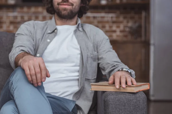 Cropped image of man sitting on sofa with hand on book at home — Stock Photo