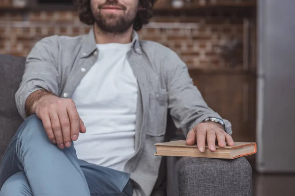 Image recadrée de l'homme assis sur le canapé avec la main sur le livre à la maison — Photo de stock