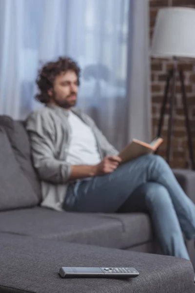 Handsome man holding book with remote control on foreground — Stock Photo