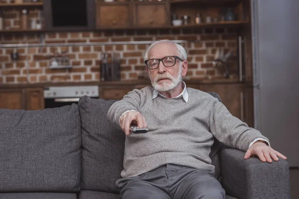 Schöner Mann mit grauen Haaren wechselt Fernsehkanäle mit Fernbedienung zu Hause — Stockfoto