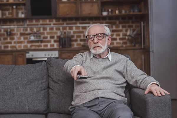 Handsome grey hair man changing tv channels with remote control at home — Stock Photo