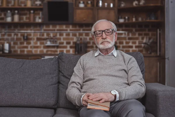 Pensive handsome grey hair man holding book and looking at camera — Stock Photo