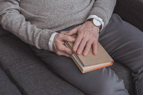 Abgeschnittenes Bild eines Mannes mit grauen Haaren, der Buch zu Hause hält — Stockfoto