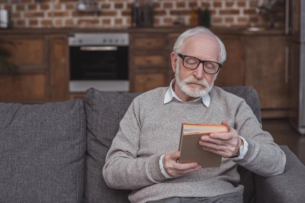 Schöner älterer Mann sitzt auf Sofa und hält Buch — Stockfoto