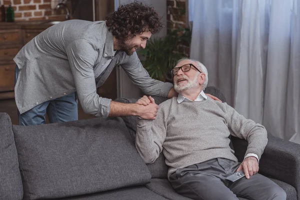 Happy adult son and senior father holding hands at home — Stock Photo