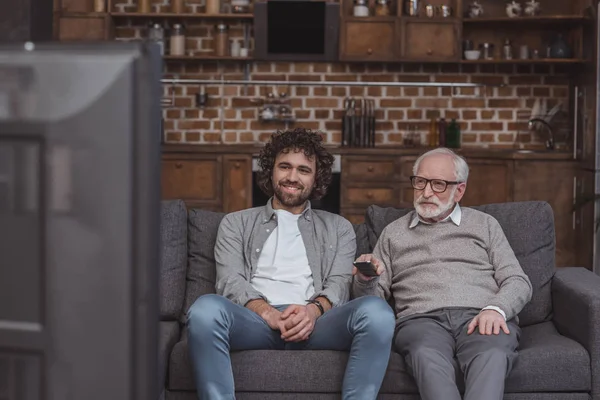 Взрослый сын и старший отец смотрят телевизор на диване дома — стоковое фото