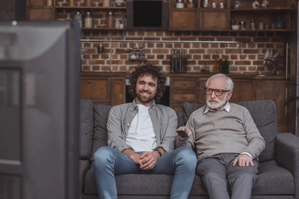 Fils adulte et père aîné regardant la télévision sur le canapé à la maison — Photo de stock