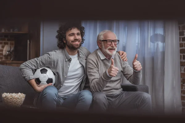 Happy adult son hugging senior father while showing thumbs up at home — Stock Photo