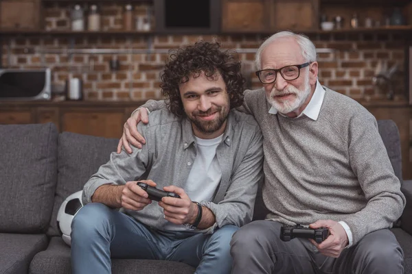 Senior Vater umarmt erwachsenen Sohn beim Videospiel zu Hause — Stockfoto