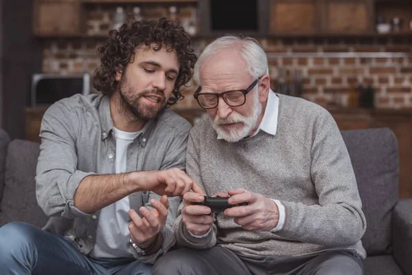 Adult son describing senior father joystick at home — Stock Photo