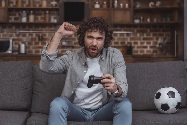 Hombre guapo mostrando sí signo mientras juega videojuego en casa - foto de stock