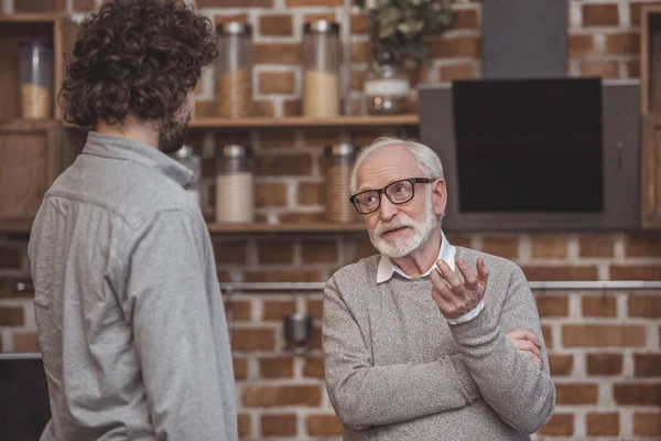 Filho adulto e pai sênior conversando em casa de cozinha — Fotografia de Stock