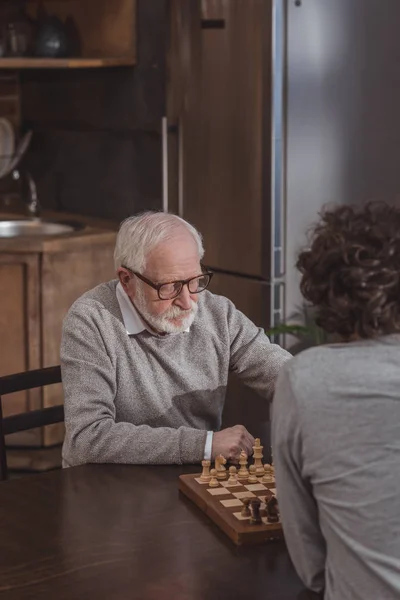Vista de ángulo alto de hijo adulto y padre mayor jugando ajedrez en casa - foto de stock