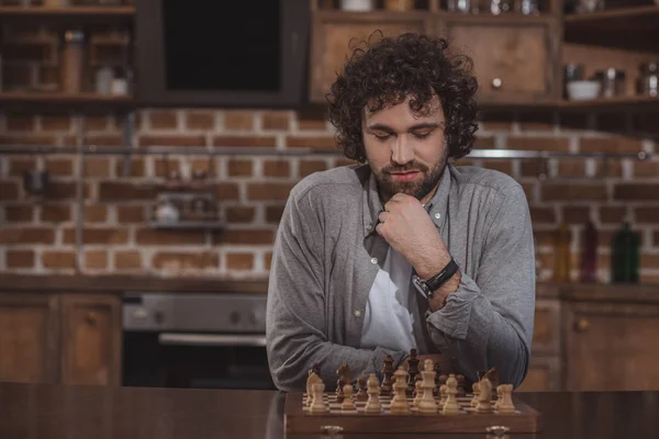 Handsome man thinking and looking at chessboard at home — Stock Photo