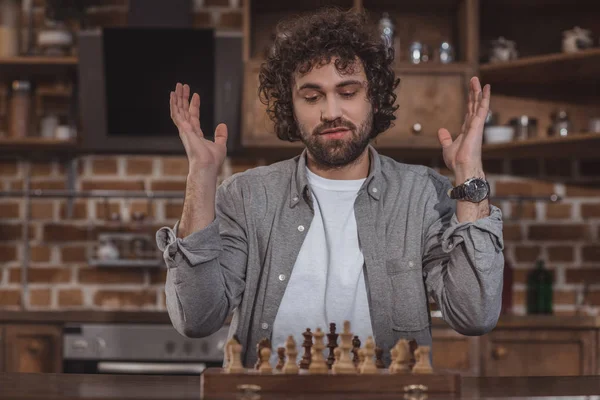 Homem bonito gesticulando e olhando para o xadrez em casa — Fotografia de Stock