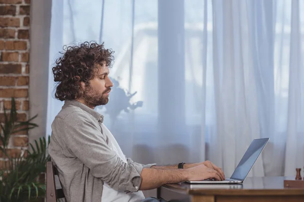 Vista lateral de homem bonito usando laptop na mesa em casa — Fotografia de Stock