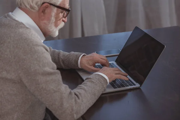 Вид сбоку красивого седовласого мужчины, использующего ноутбук дома — стоковое фото
