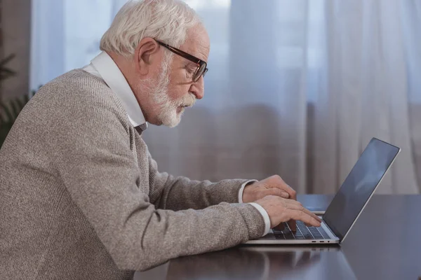 Seitenansicht eines gutaussehenden Mannes mit grauen Haaren, der zu Hause Laptop benutzt — Stockfoto