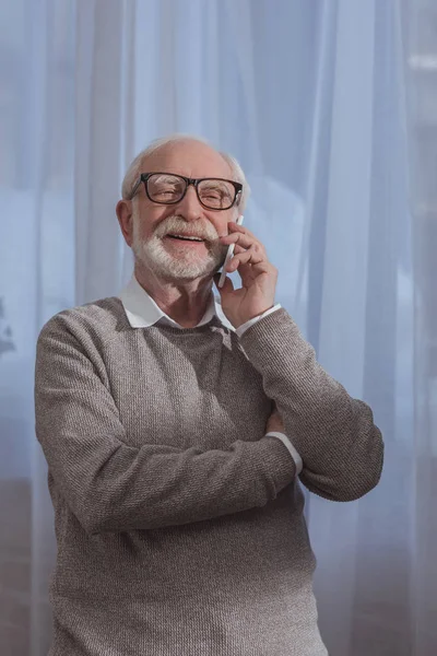 Красивый улыбающийся седой мужчина разговаривает по смартфону дома — стоковое фото