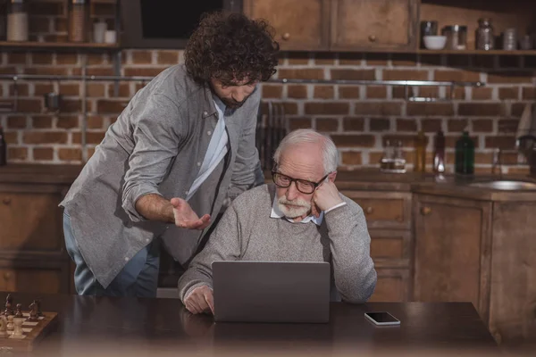 Adult son and senior father looking at laptop at home — Stock Photo