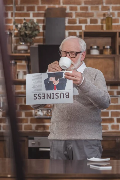 Красивый седой мужчина пьет кофе и читает деловую газету дома — стоковое фото