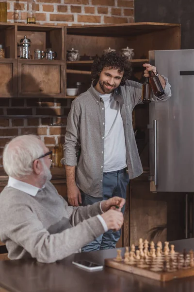 Hijo adulto proponiendo cerveza a padre mayor en casa - foto de stock