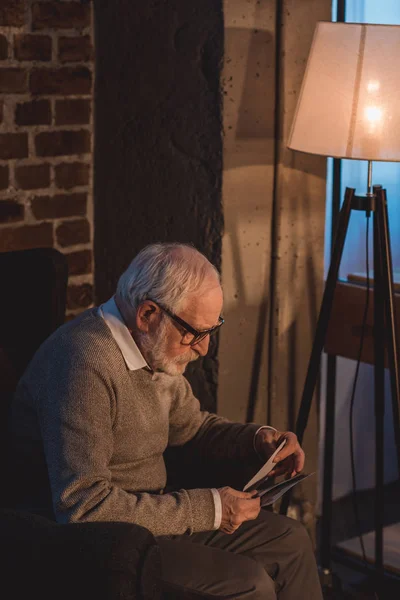 Seitenansicht eines gutaussehenden Mannes mit grauen Haaren, der im Sessel sitzt und zu Hause alte Fotos betrachtet — Stockfoto