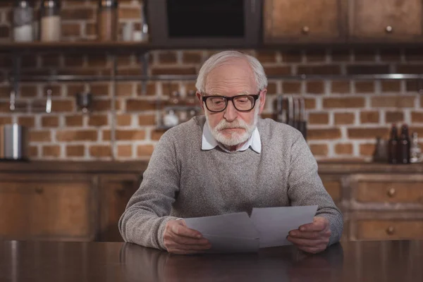 Beau homme aux cheveux gris assis à table et regardant des photos à la maison — Photo de stock