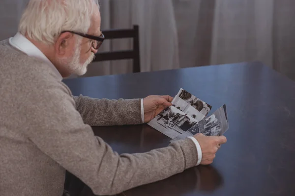 Side view of grey hair man sitting at table and looking at photos at home — Stock Photo