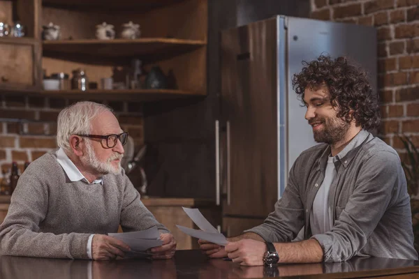 Smiling adult son and senior father looking at old photos at home — Stock Photo