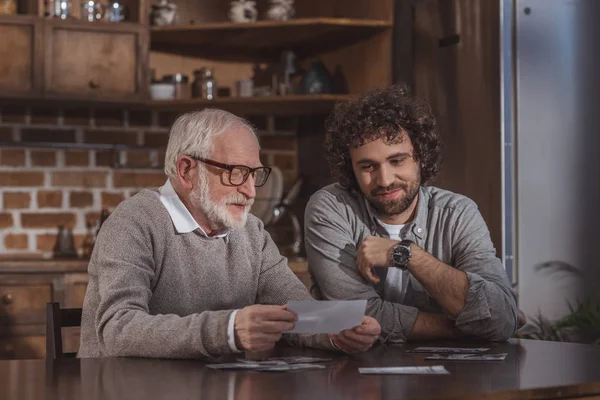 Fils adulte et père aîné regardant de vieilles photos à la maison — Photo de stock