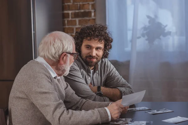 Felice figlio adulto e padre anziano guardando vecchie foto a casa — Foto stock