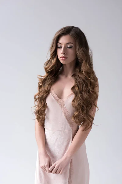 Modelo encaracolado atraente com cabelo longo posando em vestido rosa, isolado em cinza — Fotografia de Stock