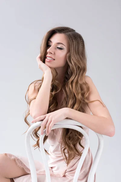 Happy tender girl with long hair posing on chair, isolated on grey — Stock Photo