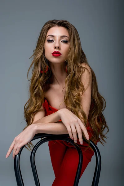 Attractive girl with long hair posing at chair, isolated on grey — Stock Photo