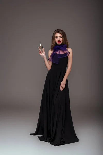Schönes Mädchen posiert in schwarzem Kleid mit Champagnerglas für Modeshooting, isoliert auf grau — Stockfoto