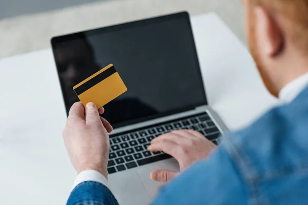 Hombre que paga por la compra en línea con tarjeta de crédito y portátil - foto de stock