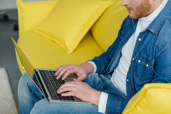 Freelancer hombre trabajando en el ordenador portátil mientras está sentado en el sofá - foto de stock