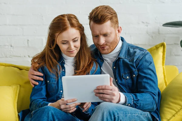 Hombre y mujer mirando la pantalla de la tableta mientras están sentados en el sofá - foto de stock