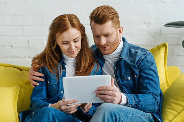 Homme et femme regardant l'écran de la tablette assis sur le canapé — Photo de stock