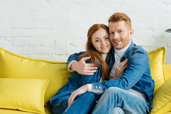 Abbracciare una coppia sorridente seduta sul divano — Foto stock