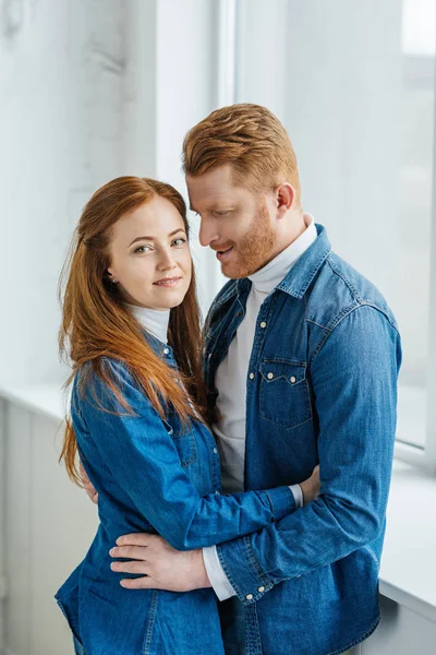 Attraktives glückliches Paar, das sich am Fenster umarmt — Stockfoto