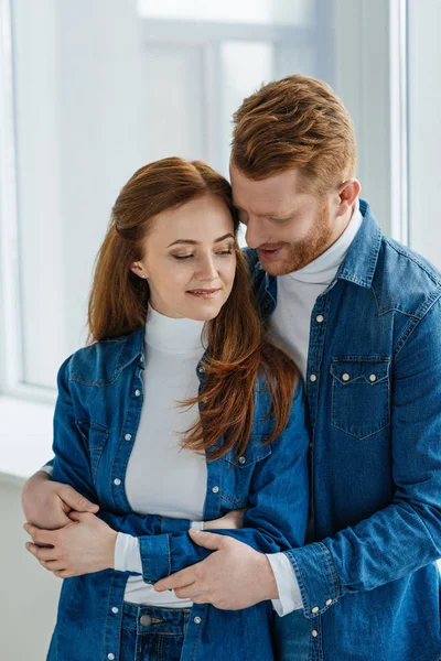 Redhead woman and man embracing by window — Stock Photo