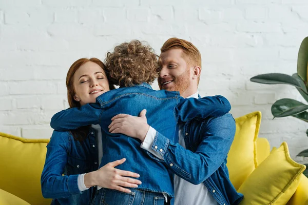 Smiling parents and son embracing on sofa in room — Stock Photo