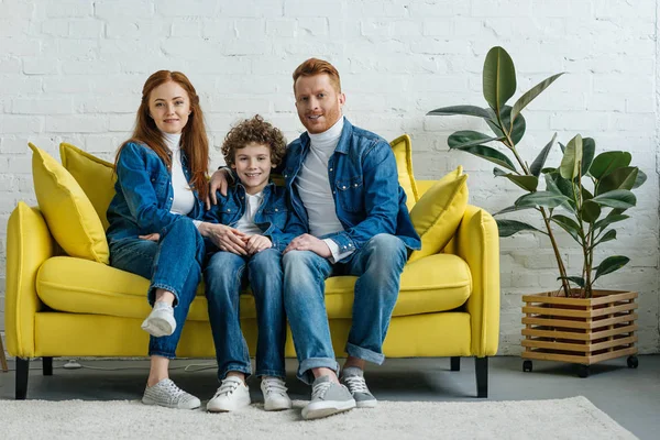 Sonrientes padres e hijo sentado en el sofá en la habitación - foto de stock