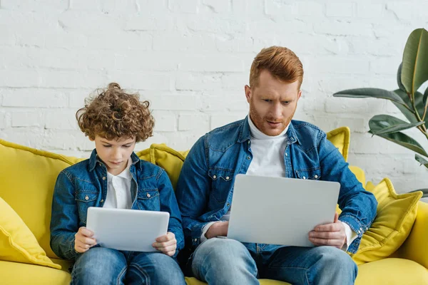 Filho concentrado e reunir olhando para laptop e tablet digital — Fotografia de Stock