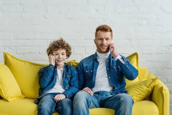 Padre e hijo hablando en teléfonos inteligentes mirando a la cámara - foto de stock